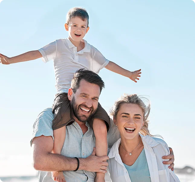 A cheerful family outdoors in Katy TX: a man carrying a smiling boy on his shoulders while a woman stands close beside them, all laughing and enjoying a sunny day—protected by Casillas Insurance Services.